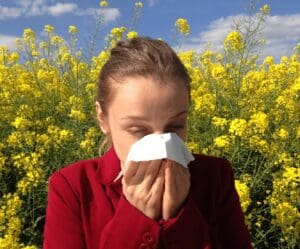 A woman in red shirt holding her nose and tissue.