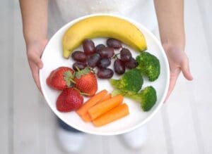 A person holding a plate of fruit and vegetables.