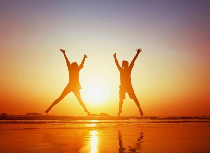 Two people jumping in the air on a beach.