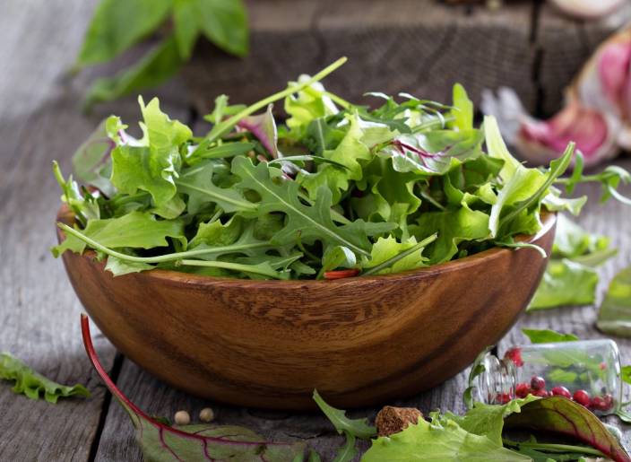 A bowl of salad sitting on top of a wooden table.